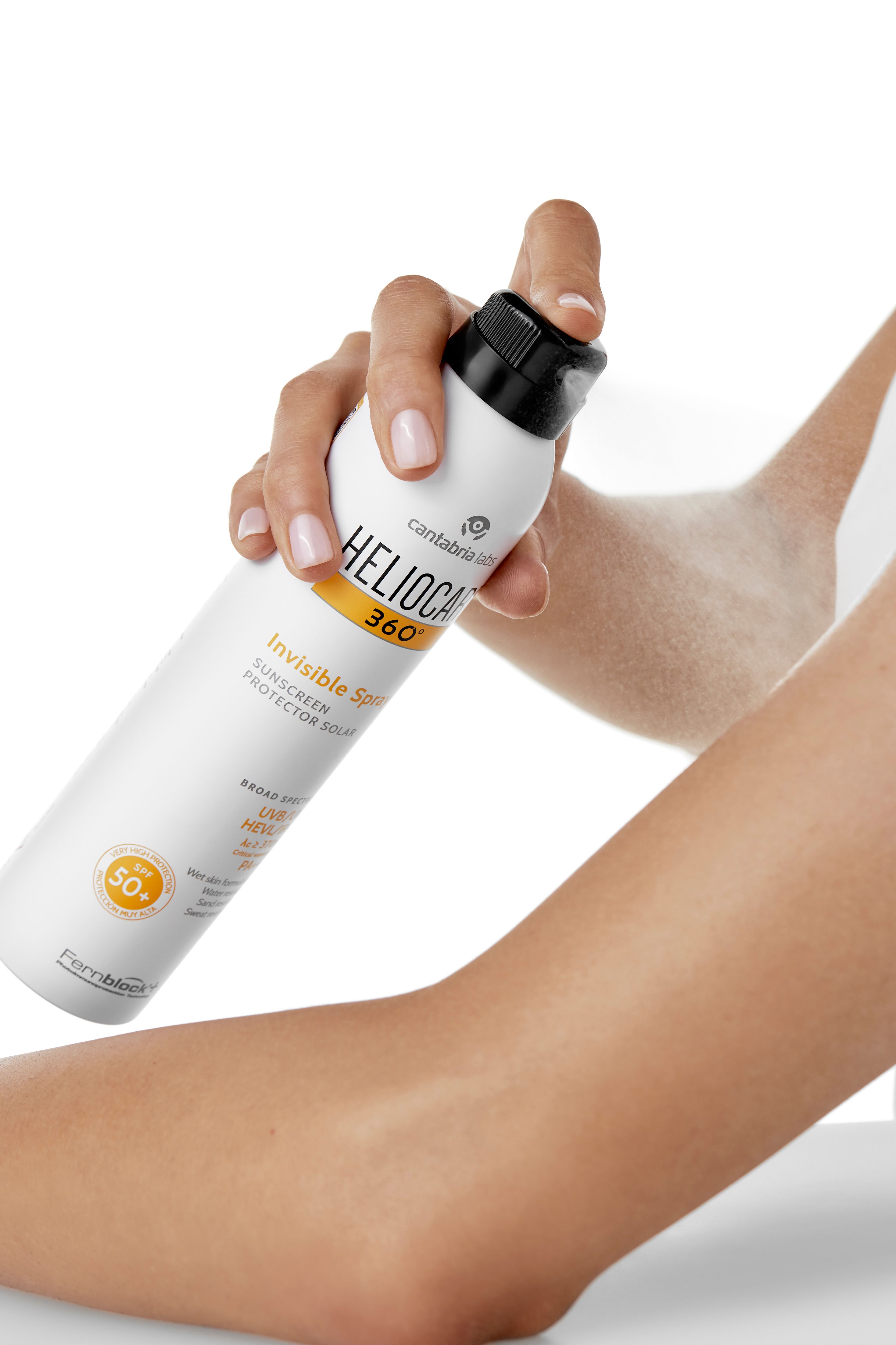 Personne vaporisant sur un bras. Spray: HELIOCARE 360° Invisible Spray, SPF 50+. Blanc, bouchon noir.