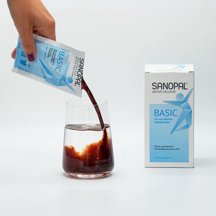 Main versant du liquide d'un sachet dans un verre. Le sachet porte la mention SANOPAL BASIC. L'emballage du produit est à côté.