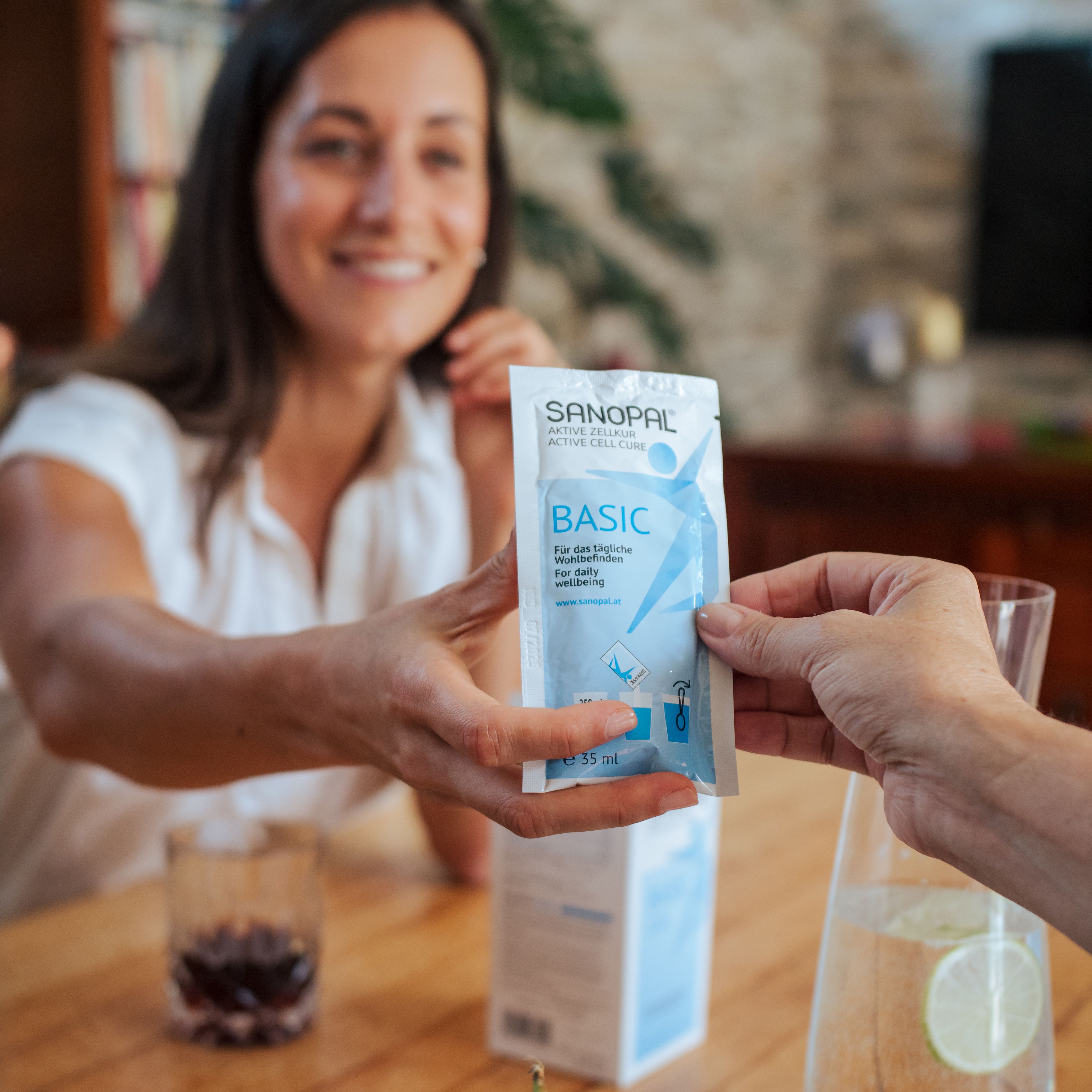 Des personnes se passent un sachet SANOPAL BASIC. Le nom du produit est sur le sachet. L'emballage du produit est à côté.