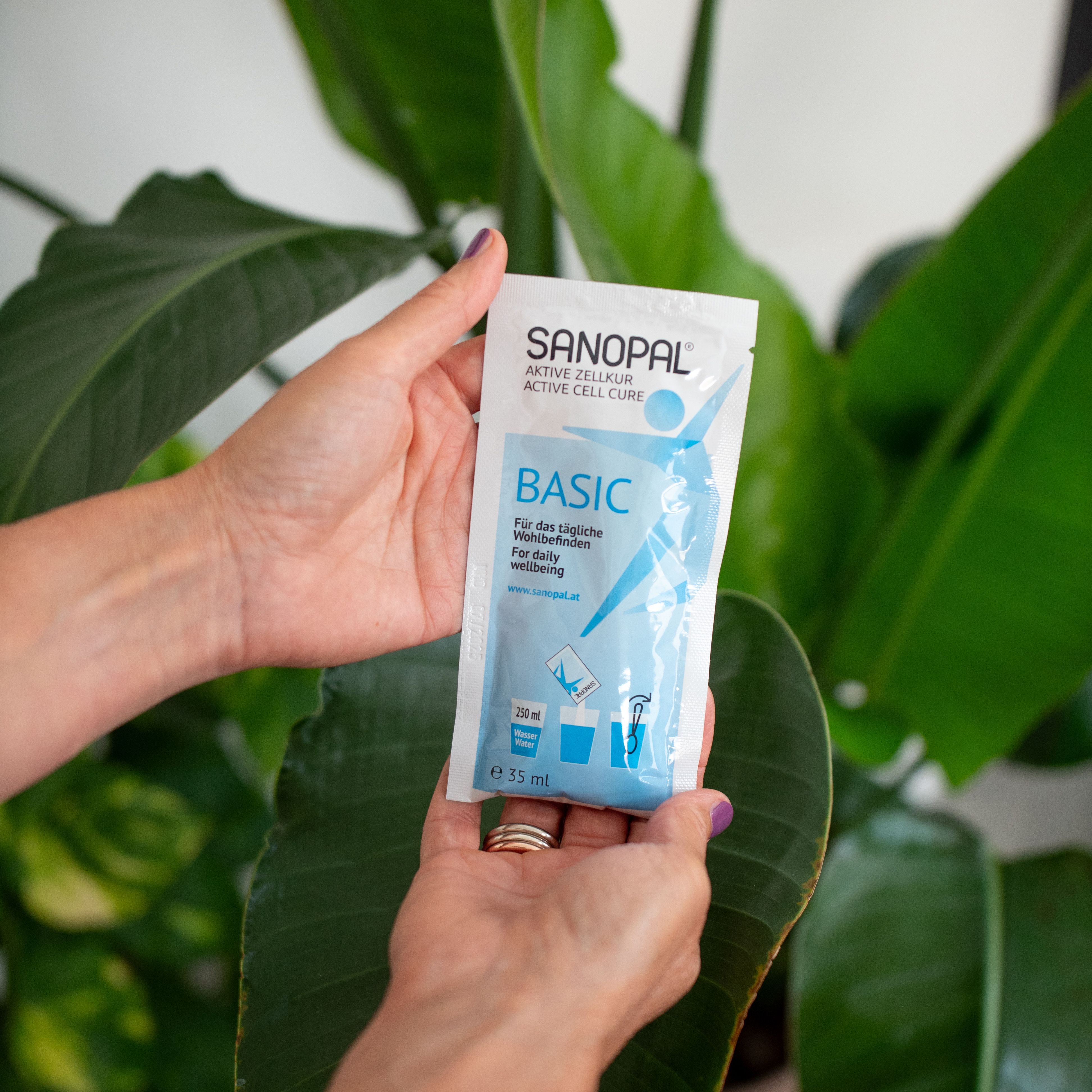 Mains tenant un sachet SANOPAL BASIC. Le nom du produit et d'autres informations sont sur le sachet. Sur fond vert.