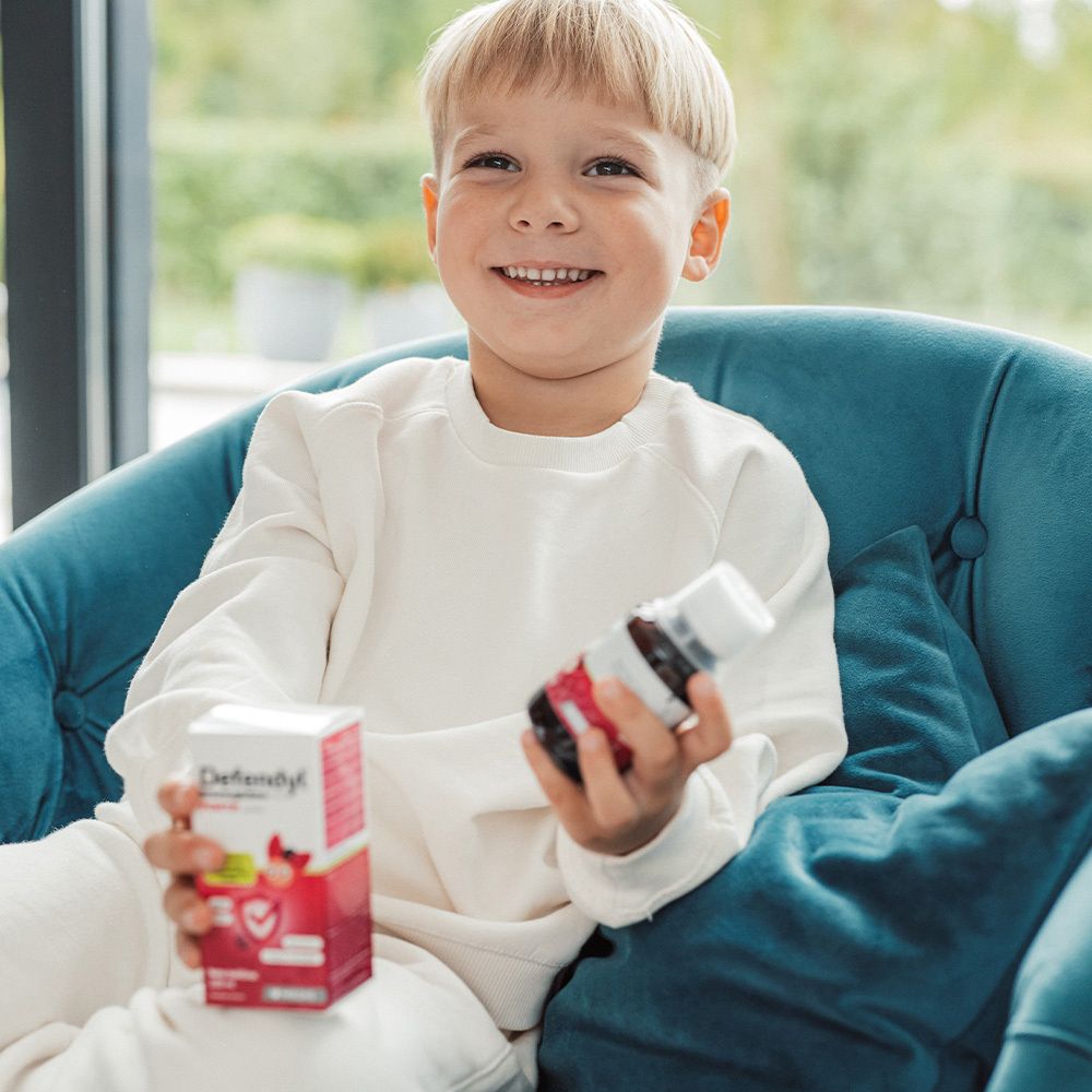 Ein Junge hält eine Flasche und eine Schachtel Defendyl-Imunoglukan P4H® FORTE. Er lächelt.