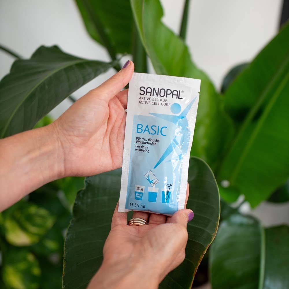 Hände halten einen Beutel. Aufschrift: SANOPAL BASIC. Im Hintergrund eine Pflanze.