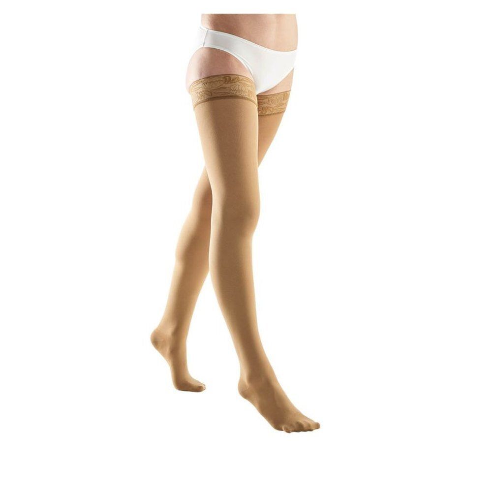 Bas de compression beiges. Pointe et bordure en dentelle. Sur fond blanc.