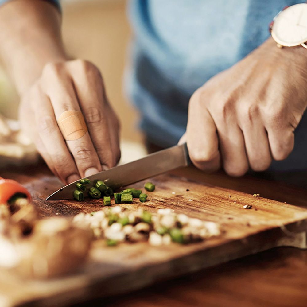 Homme coupant des légumes sur une planche en bois. Pansement sur le doigt. Cuisine en arrière-plan.