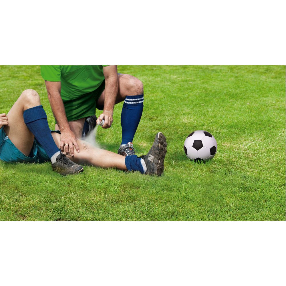 Deux personnes sur l'herbe. Une personne vaporise sur la jambe d'une autre. Ballon de football à côté.