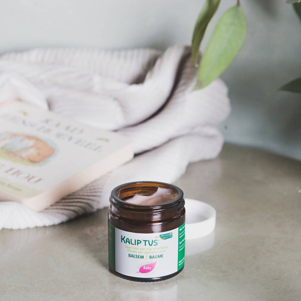 Pot brun avec couvercle blanc. Inscription: Kalip'tus, Baume pectoral, Baby. Sur une table.