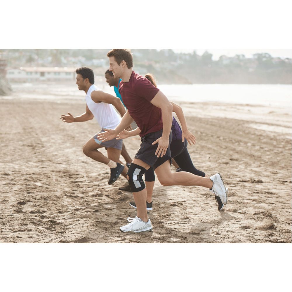 Genouillère. Noir et gris. Avec fermetures velcro. 3M™ Futuro™ Sport. Sur l'emballage, une personne porte la genouillère.