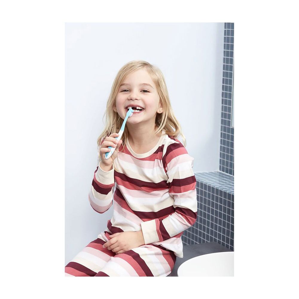 Une fille se brosse les dents avec une brosse à dents bleue. Elle est assise sur un lavabo.