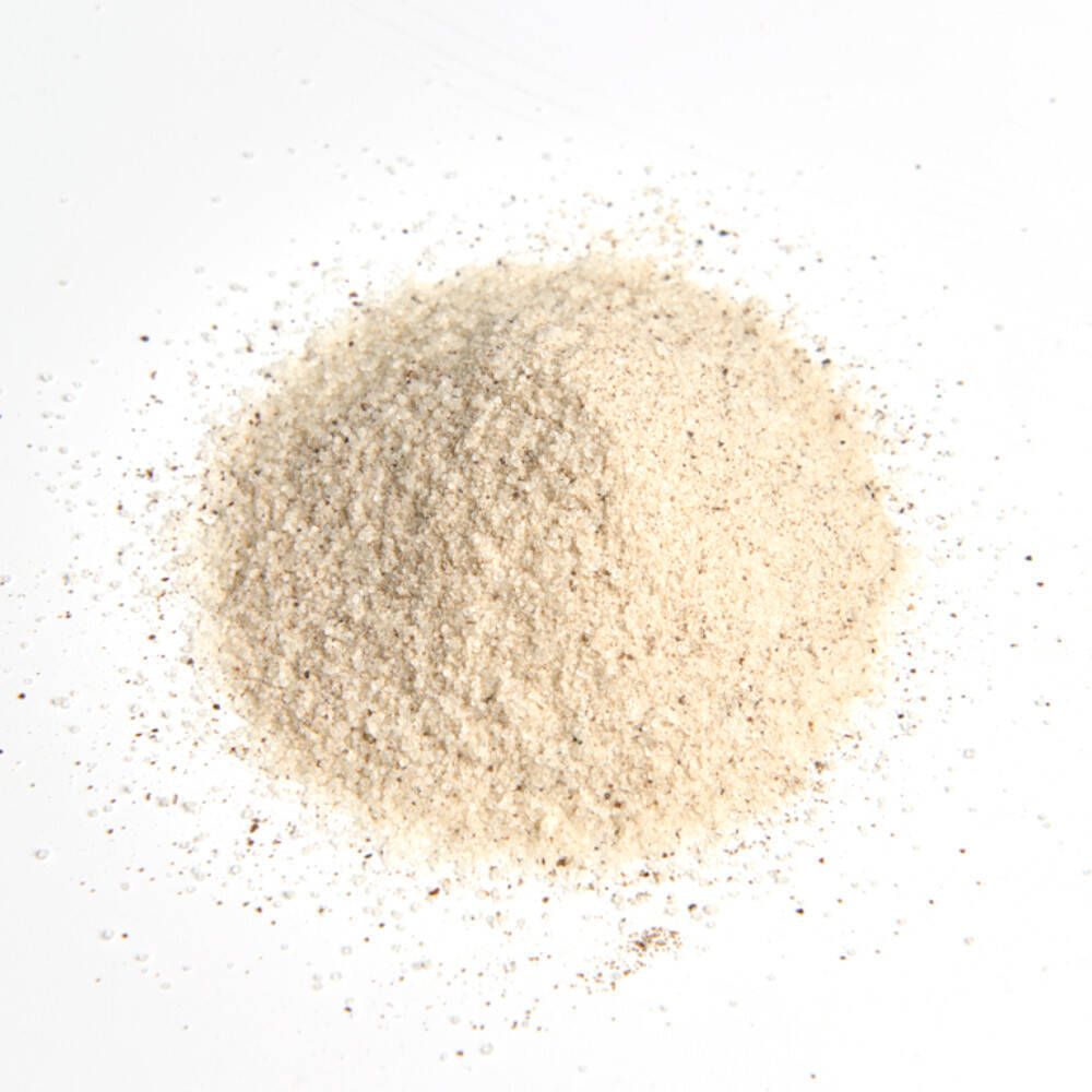 Tas de poudre brun clair sur fond blanc. Grain fin, forme légèrement irrégulière.