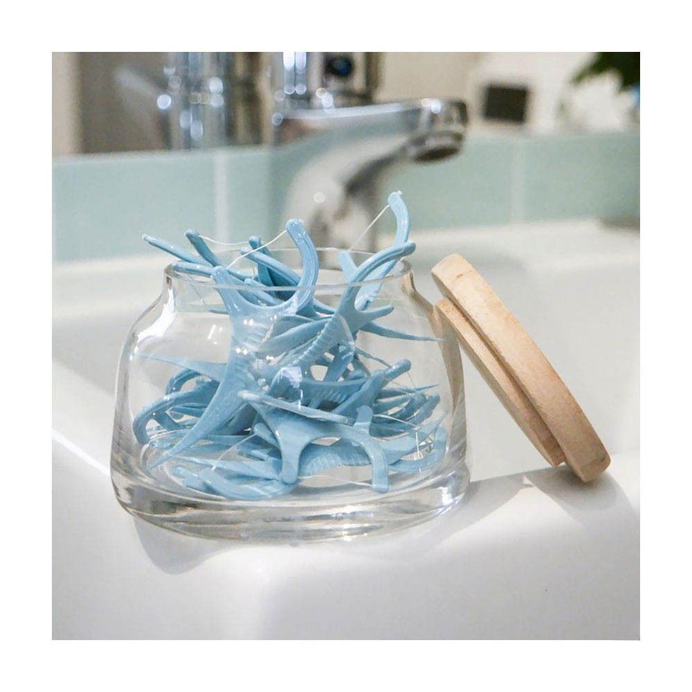 Glasbehälter mit blauen Jordan 3-in-1 Flossern. Holzpinzette daneben. Auf weißer Oberfläche.