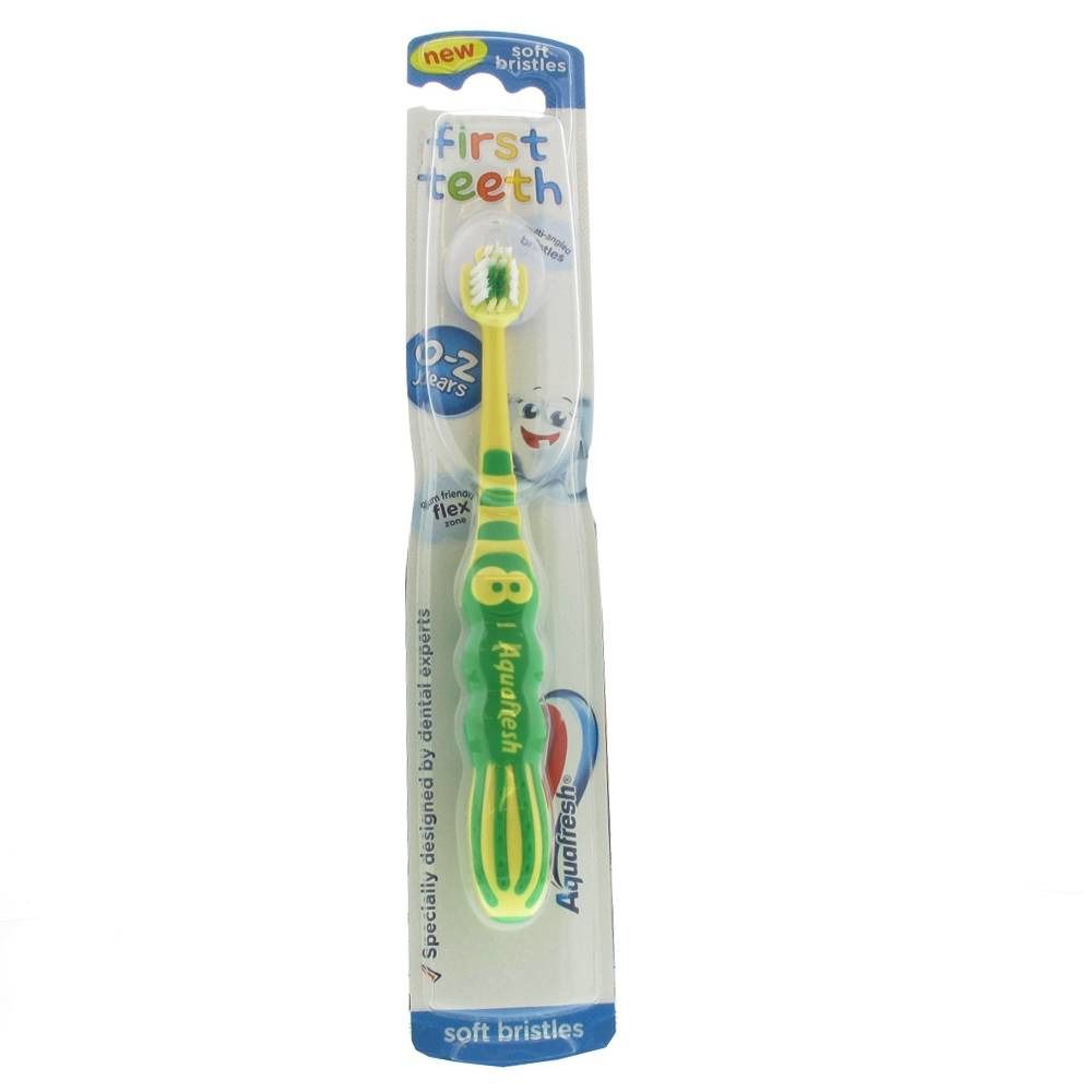 Brosse à dents verte et jaune pour premières dents dans son emballage. Avec des soies souples et l'inscription "First Teeth".