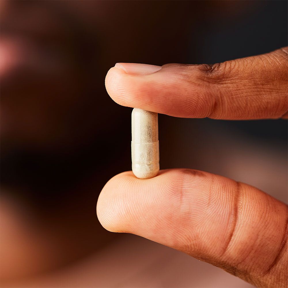 Personne tenant une gélule de vitamine C unique entre les doigts.