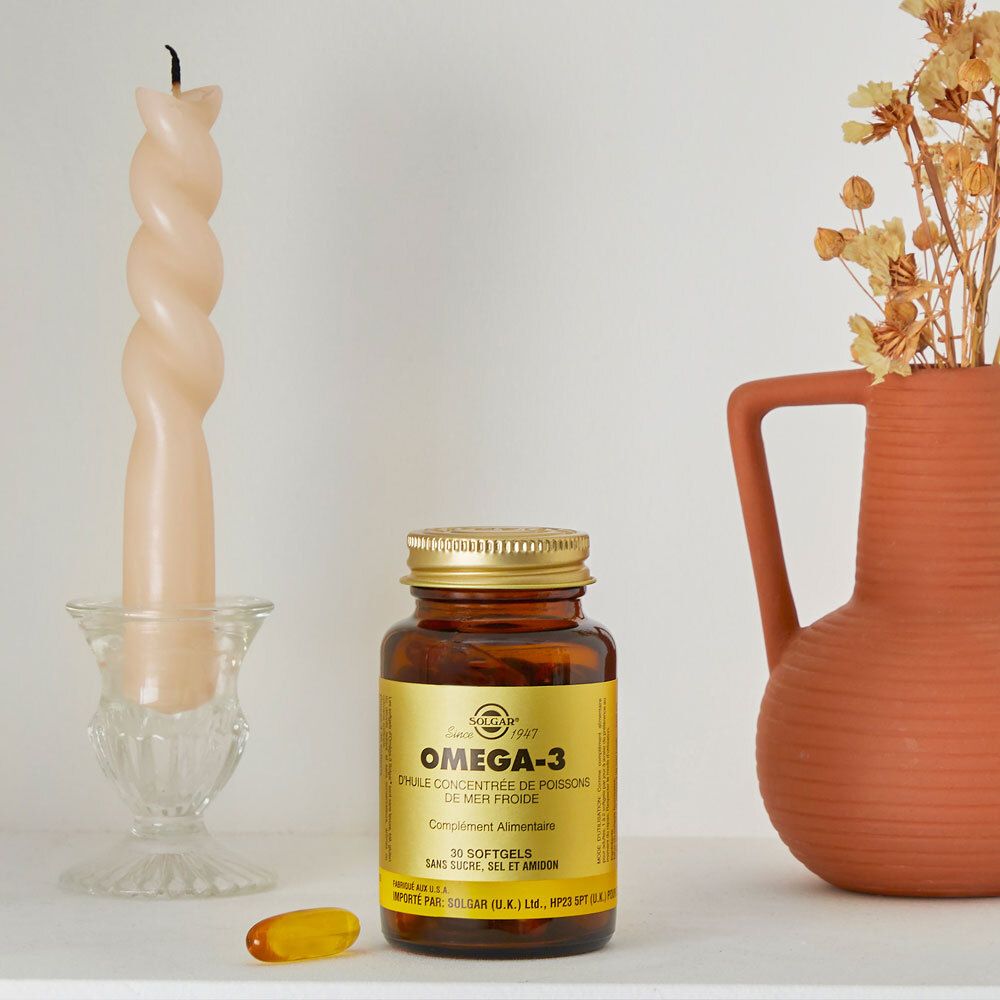 Flacon brun avec bouchon doré. Près d'une bougie et d'un vase. Une gélule à côté.