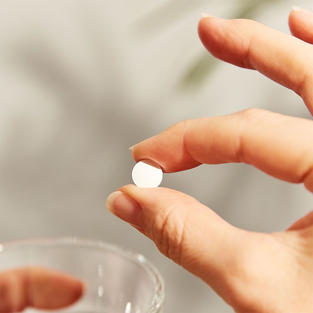 Hand hält eine einzelne weiße Tablette. Nahaufnahme.