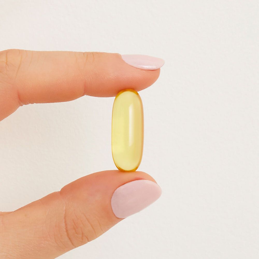 Une gélule molle jaune, tenue entre les doigts. Forme ovale claire.