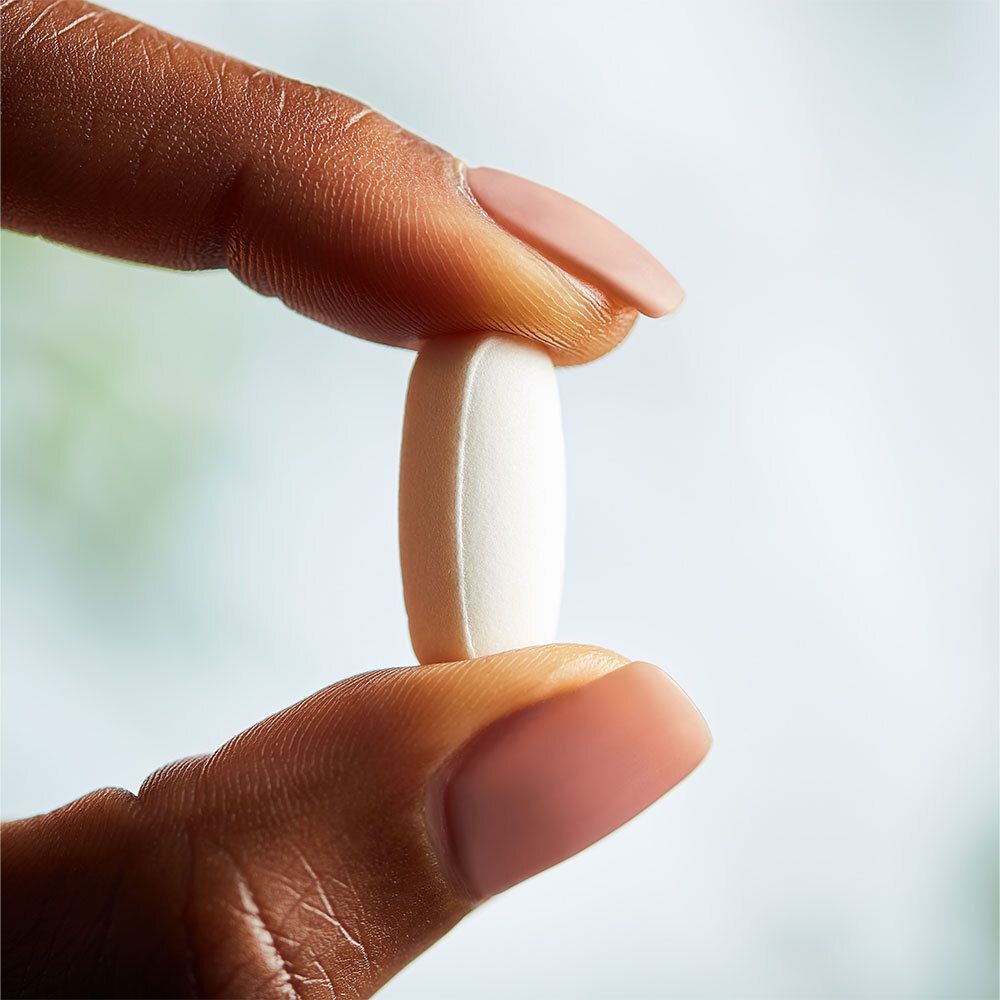 Hand hält eine weiße, ovale Tablette. Fingernägel rosa lackiert. Nahaufnahme.