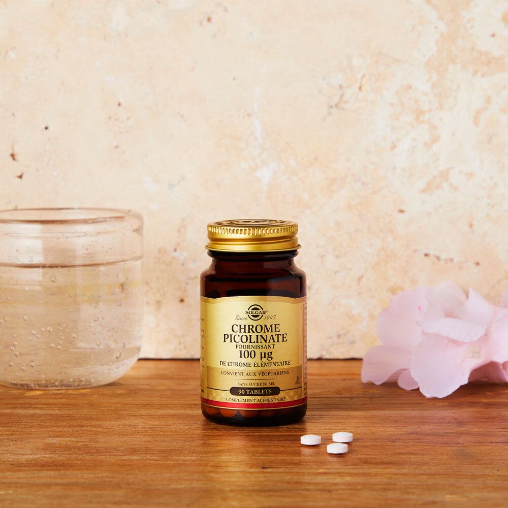 Flacon brun avec comprimés sur surface en bois. Verre d'eau et fleur en arrière-plan.