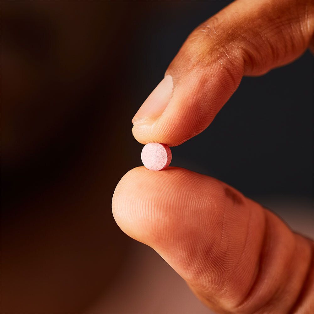 Comprimé rose tenu entre deux doigts. Gros plan.