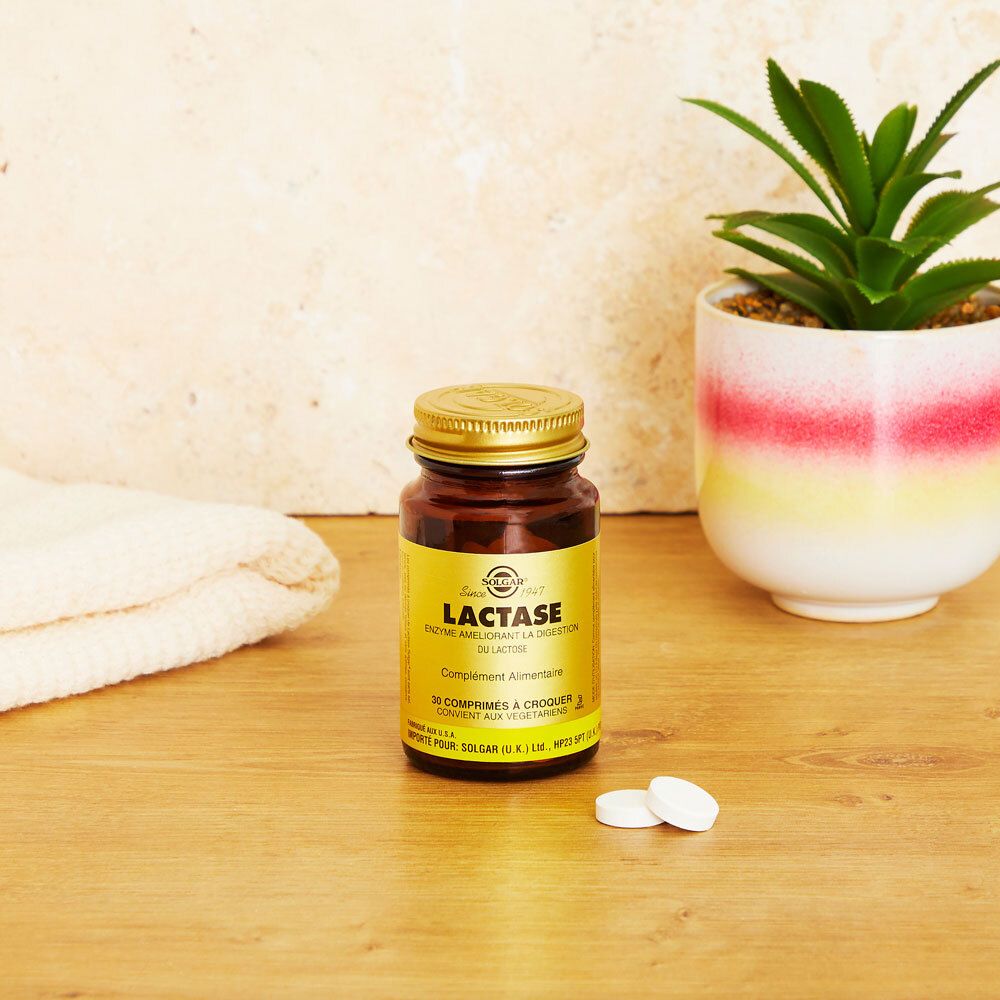 Braune Glasflasche mit goldfarbenem Deckel und Etikett. Zwei Tabletten liegen daneben. Hintergrund: Tisch und Pflanze.