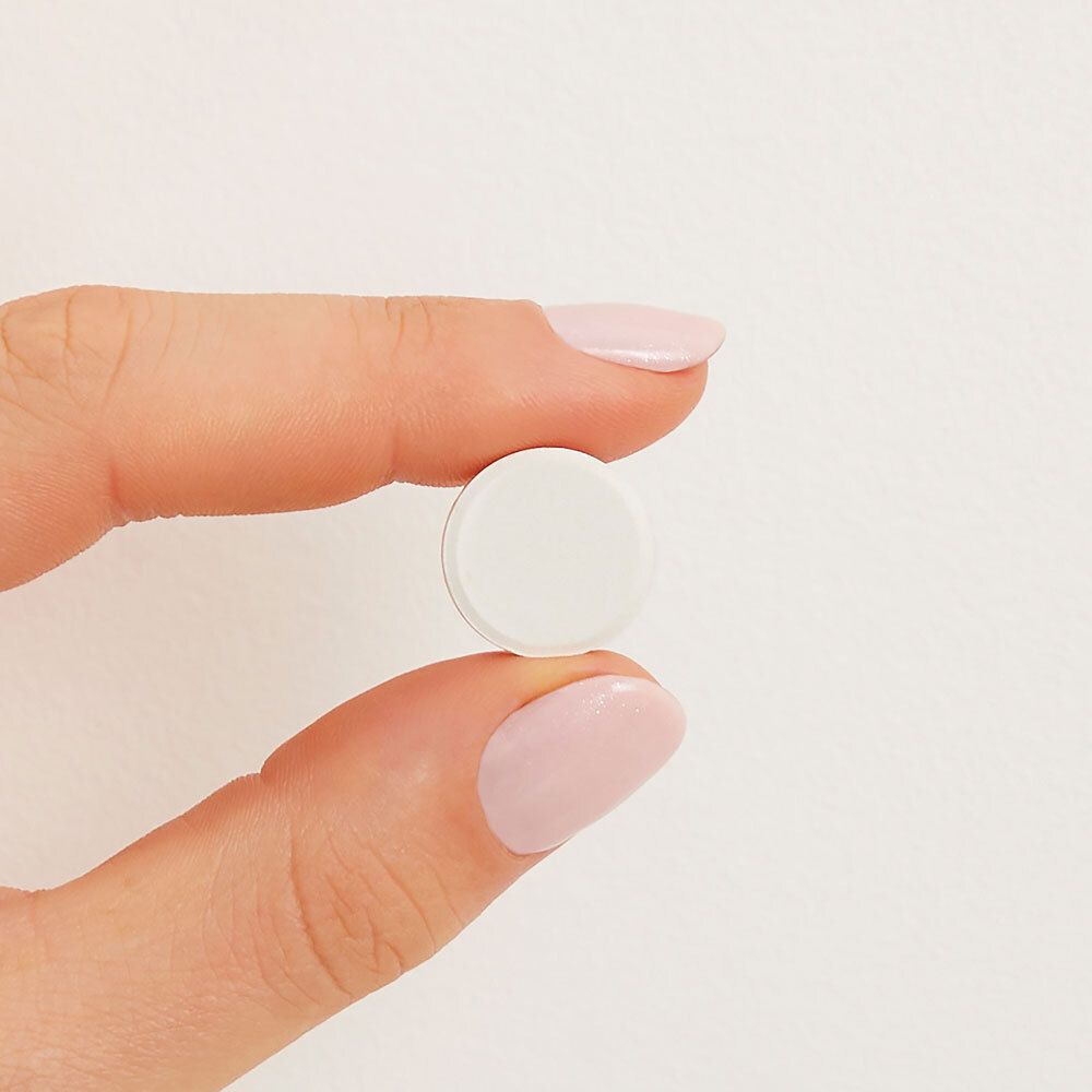 Eine Tablette, weiß und rund, wird von einer Hand gehalten. Hintergrund: weiß.