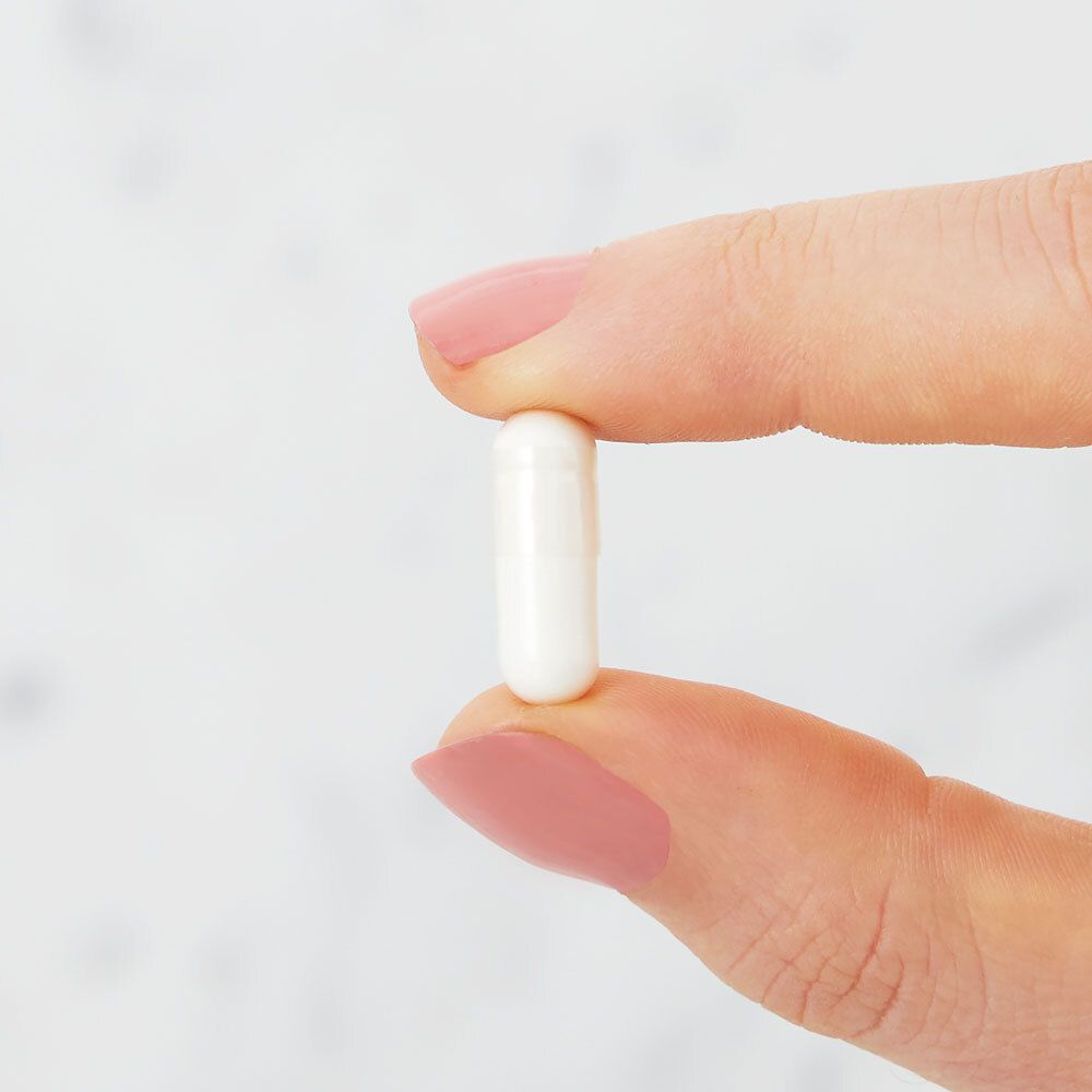 Eine weiße Kapsel zwischen zwei Fingern. Rosa lackierte Fingernägel.