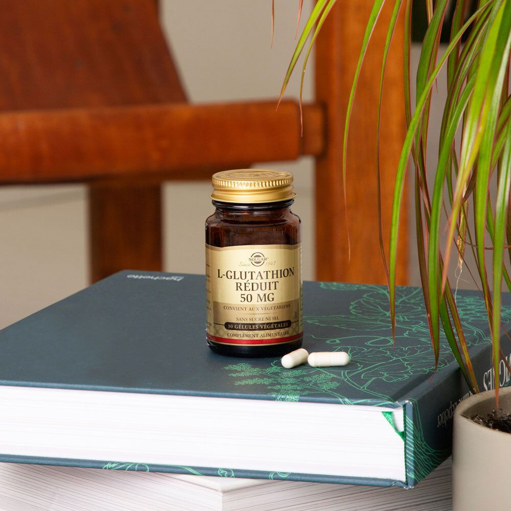 Braune Flasche mit Kapseln auf einem Buch. Pflanze im Hintergrund.