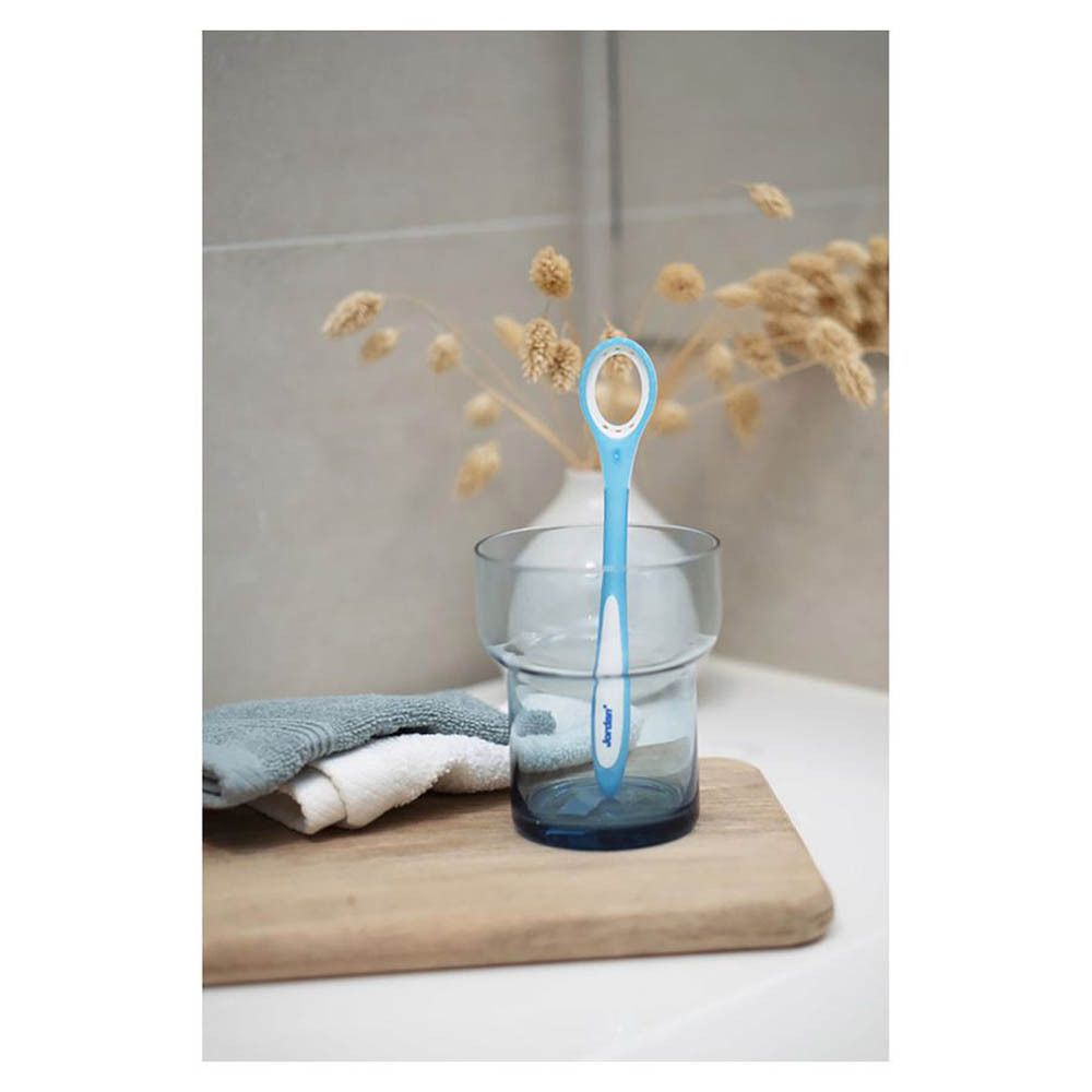 Blauer Zungenreiniger in einem Glas. Steht in einem Glas Wasser. Auf einem Holzbrett. Im Badezimmer.