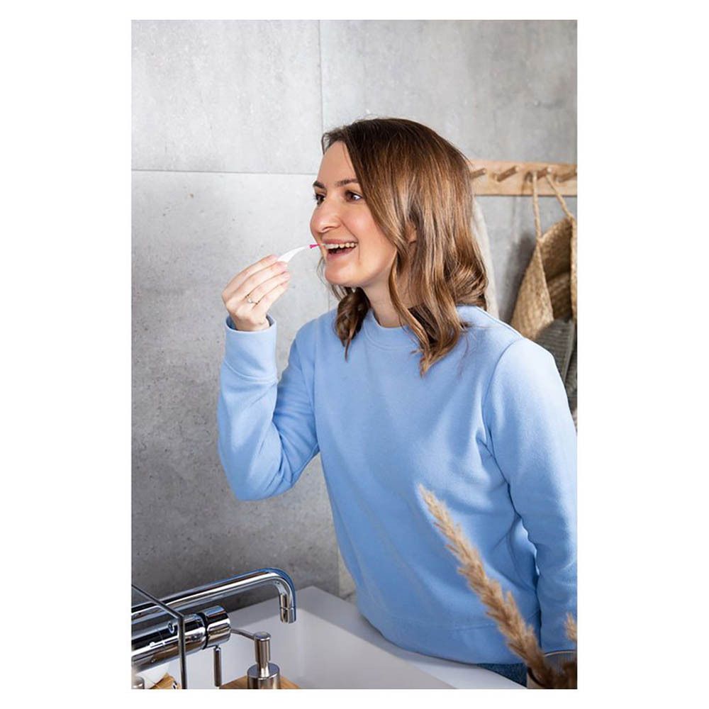 Frau putzt sich die Zähne mit einer Interdentalbürste. Badezimmerhintergrund. Produkt nicht im Detail erkennbar.