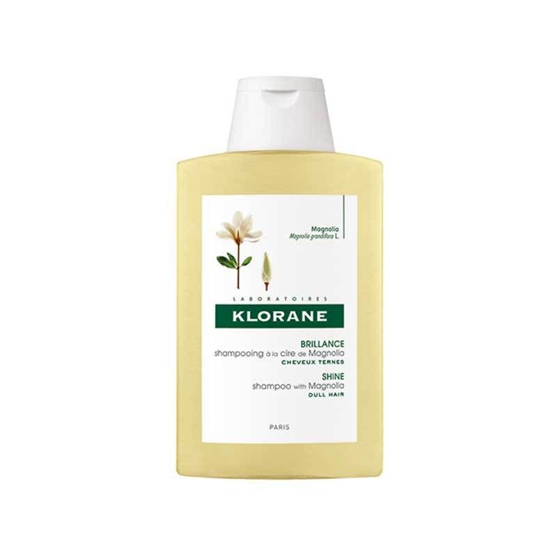 Flacon de shampooing Klorane à la cire de magnolia. Flacon jaune avec bouchon blanc. Étiquette avec informations et fleur de magnolia.