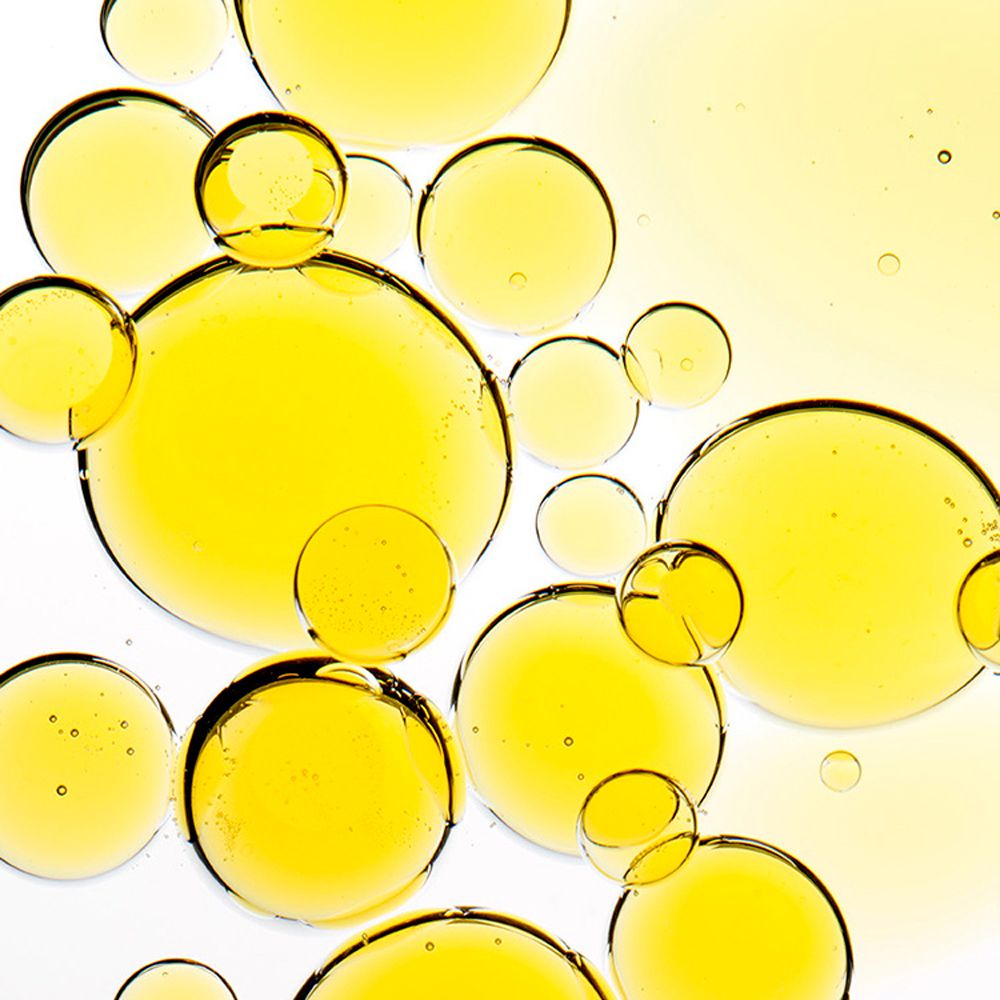 Gros plan de gouttelettes d'huile jaune sur fond blanc. Formes rondes, tailles variées.