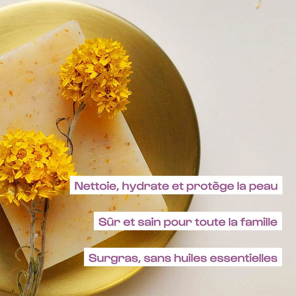 Pain de savon de couleur jaune, entouré de fleurs jaunes. Texte : Nettoie, hydrate et protège la peau.