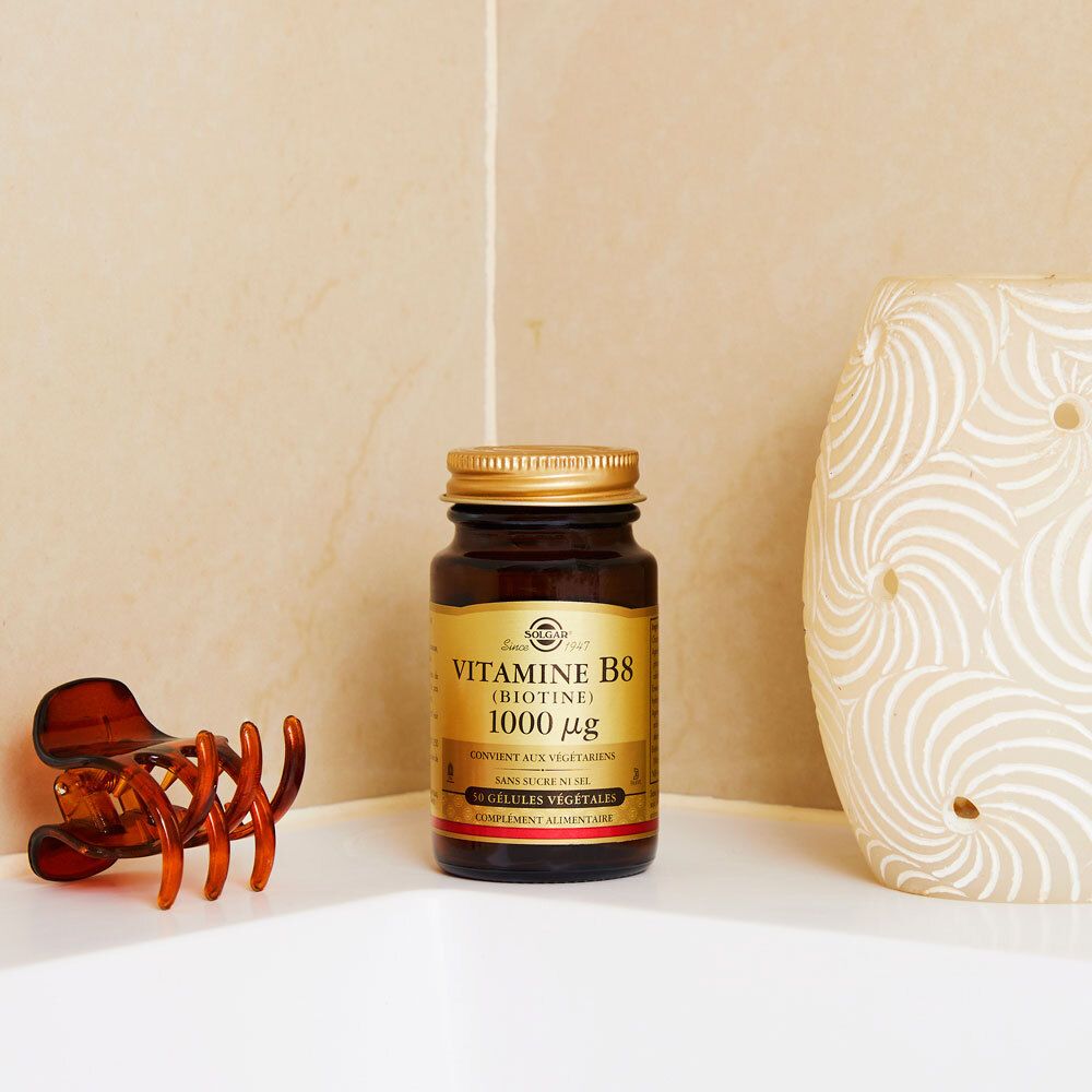 Flacon brun, bouchon doré. Posé sur une surface blanche, à côté d'une pince à cheveux.