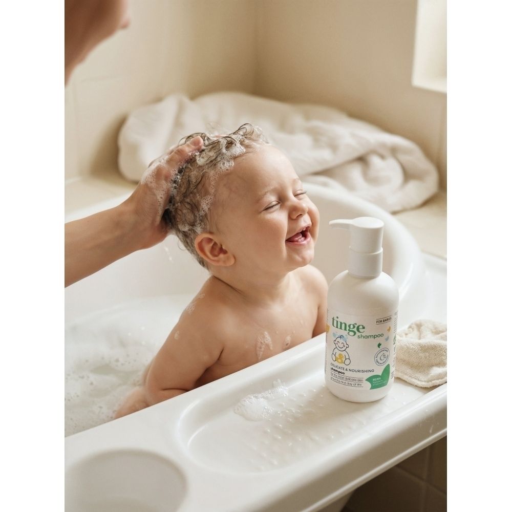 Flacon blanc avec étiquette verte. Inscription : tinge for babies Shampoo. Le produit est versé dans la main.