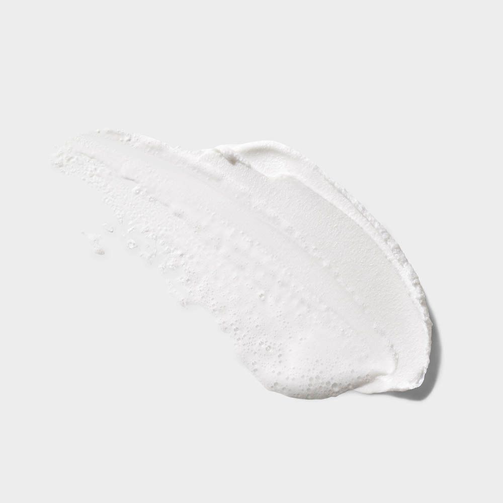 Weiße Creme-Textur mit kleinen Bläschen auf grauem Hintergrund.