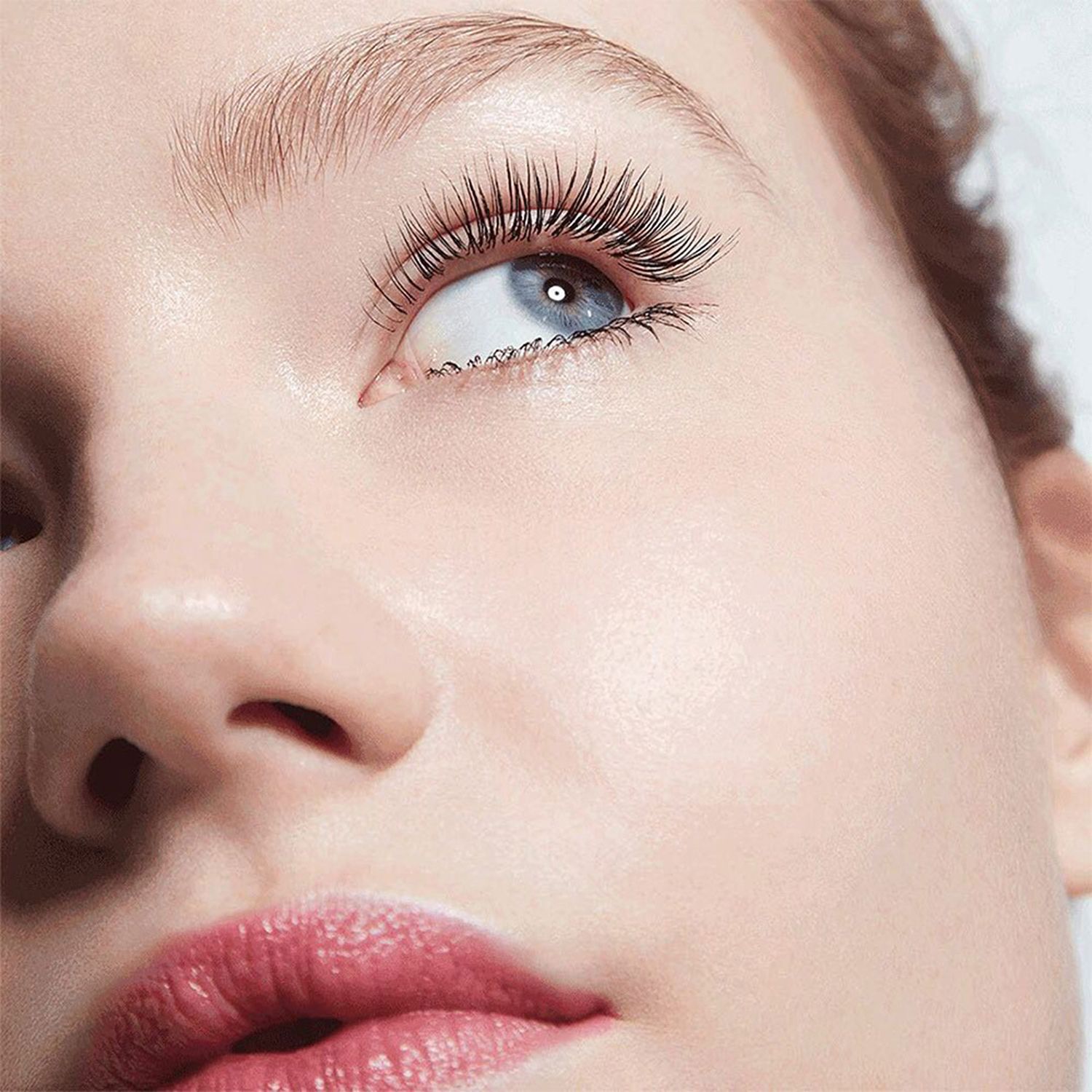 Nahaufnahme eines Gesichts mit langen, getuschten Wimpern. Roter Lippenstift.