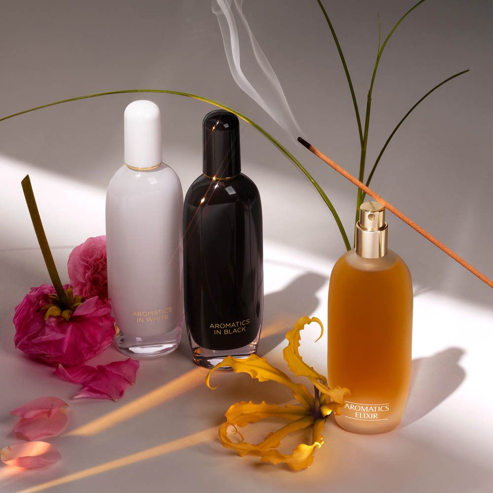 Drei Clinique Aromatics Elixir Parfümflaschen, eine davon brennt.