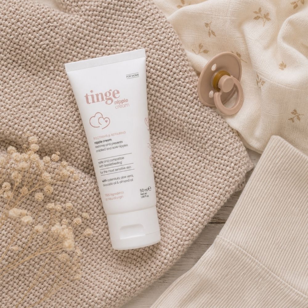 Tube de crème sur une couverture avec sucette et vêtements. Nom du produit et inscription: nipple cream.