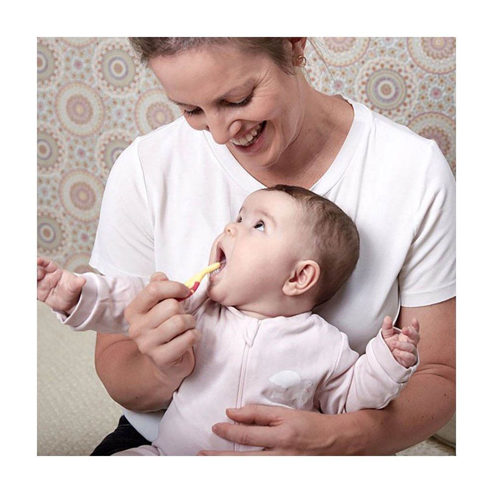 Bébé avec brosse à dents jaune dans la bouche. Personne tenant le bébé. Brosse à dents avec manche rose.