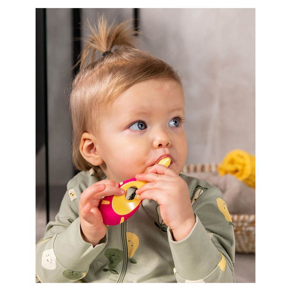 Baby mit rosa-gelber Zahnbürste im Mund. Baby hält Zahnbürste selbst. Gelber Griff.