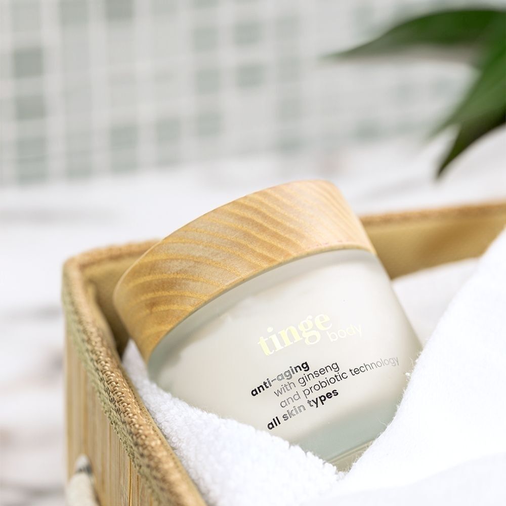 Tinge Bodylotion Anti-Aging dans un panier avec une serviette.