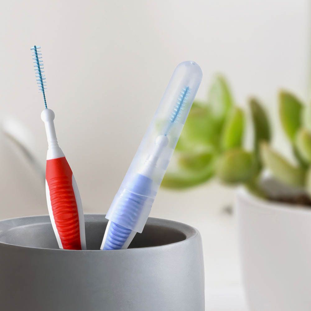 Deux brossettes interdentaires dans un gobelet. Une brosse rouge et une bleue avec étui de protection.