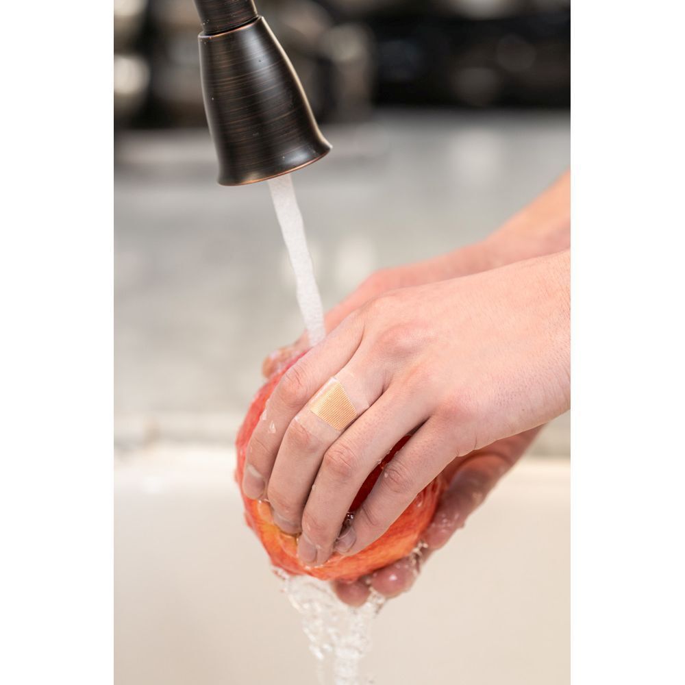 Pansement Nexcare aqua clear waterproof sur la main sous l'eau courante.
