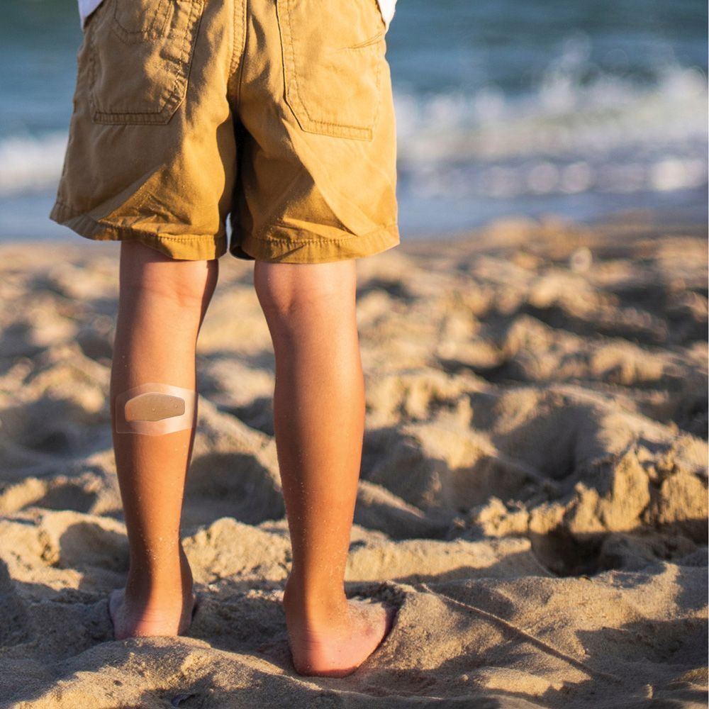 Enfant avec pansement Nexcare aqua clear MAXI sur la jambe. Sur la plage.