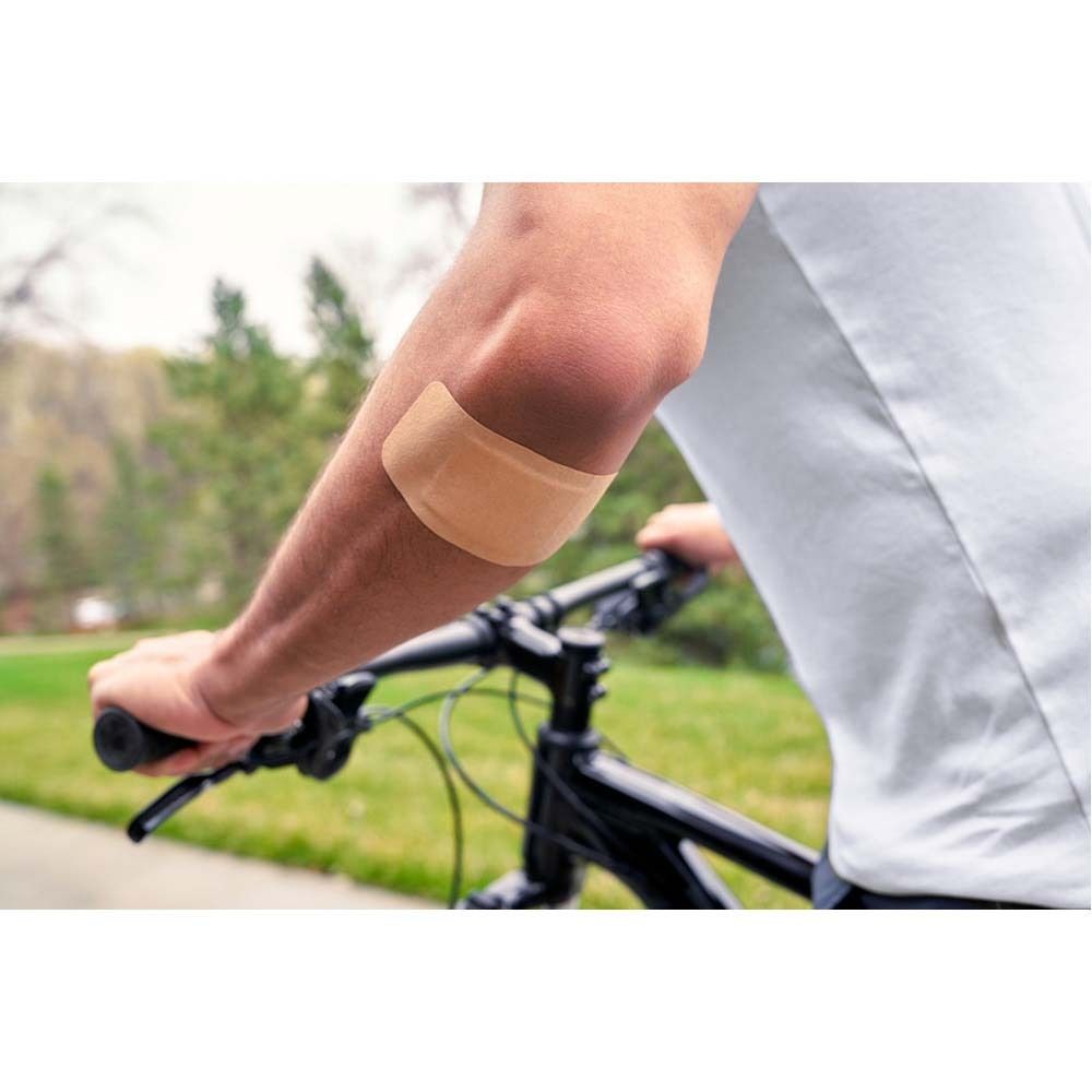 Nexcare Ultra Stretch MAXI Pflaster. Beige, rechteckig mit weißem Wundkissen. Pfeil zeigt Richtung.