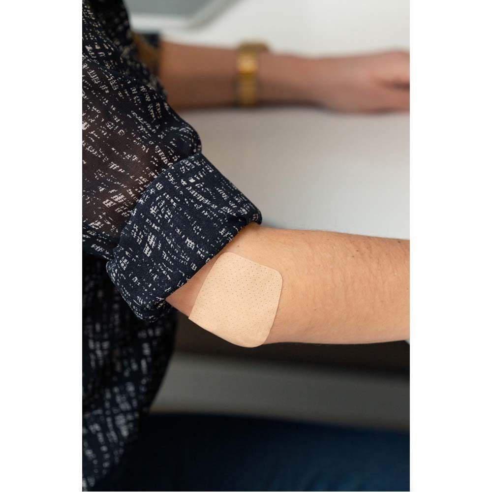 Person mit Pflaster am Knie. Pflaster ist beige und rechteckig. Person steht auf einem Fußball.