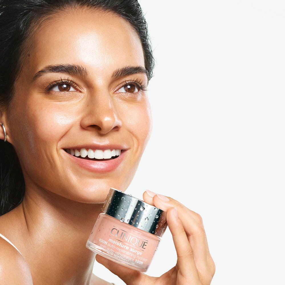 Frau hält Clinique Moisture Surge Gesichtscreme in einem Glasbehälter mit silbernem Deckel.