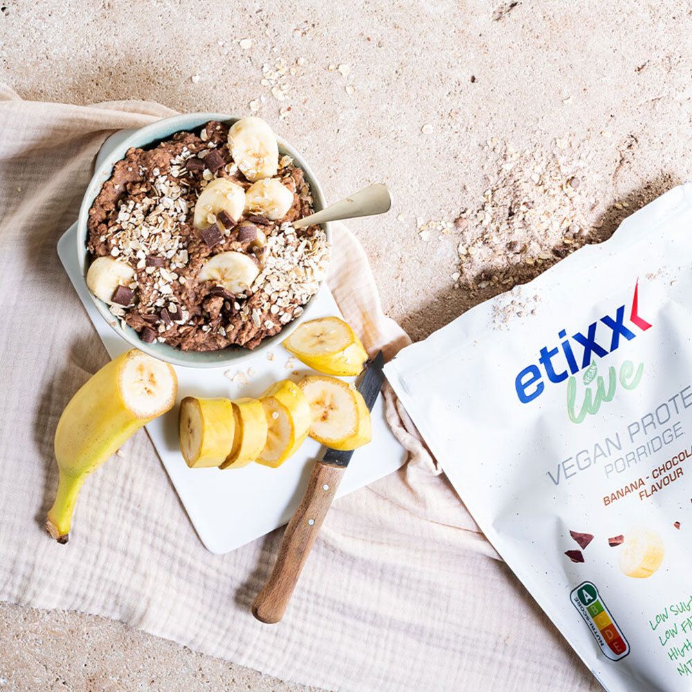 Bol de porridge avec tranches de banane et morceaux de chocolat. À côté : sachet de porridge protéiné végétalien "etixx live", banane, couteau.