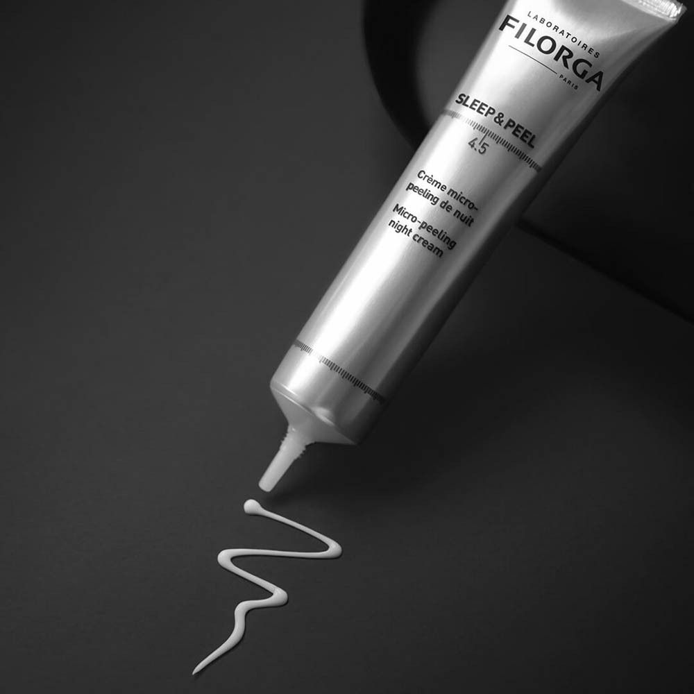 Tube argenté Filorga Sleep & Peel 4.5. Trace de produit sur fond noir.