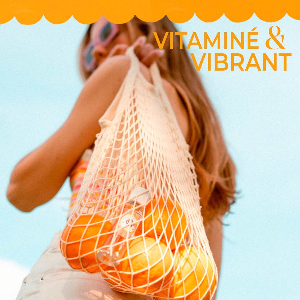 Femme avec un sac de courses plein d'oranges. Texte: Vitaminé & Vibrant.