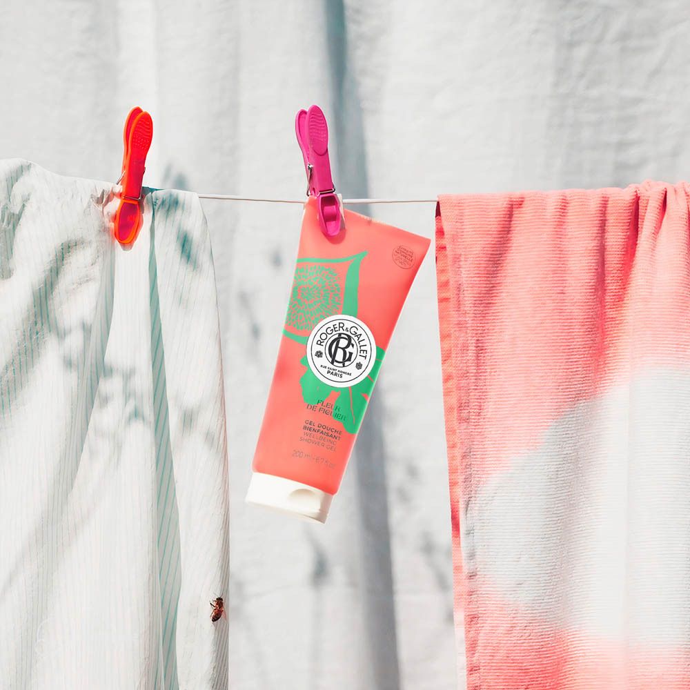 Tube de gel douche suspendu à un fil à linge avec des pinces à linge. Tube rose avec design vert. Texte: Roger & Gallet.